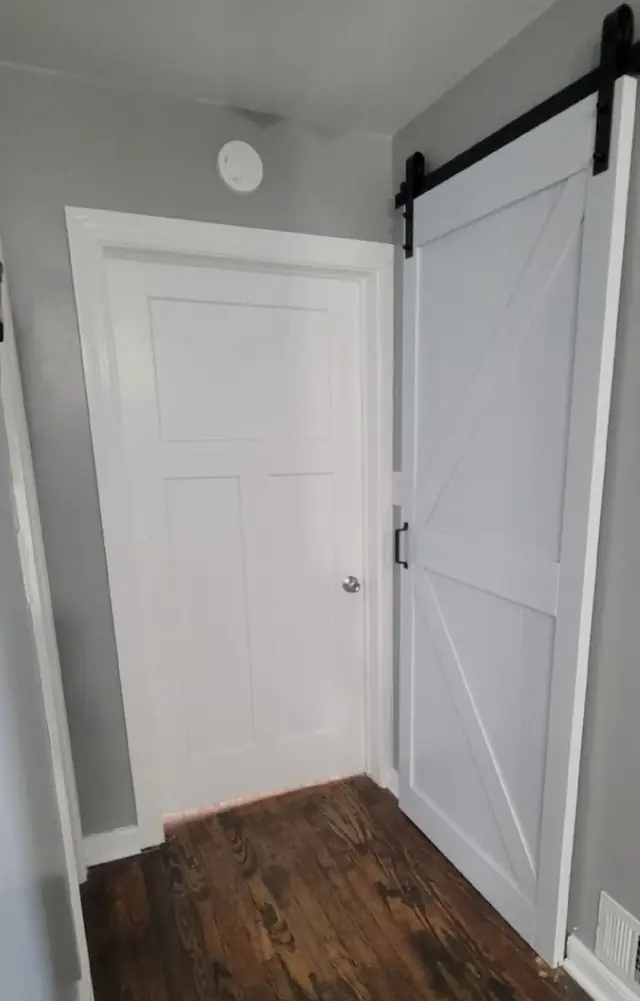 A new white panel door in a former archway and a white barn door on a black track