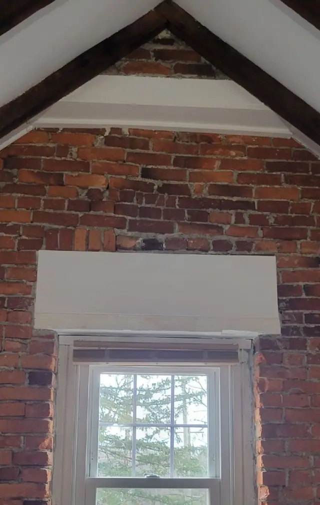 A double-hung window in an exposed brick wall, finished with new white trim and a white valance box