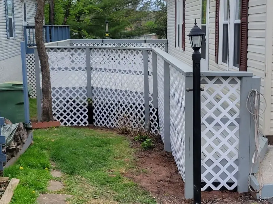 A new white lattice skirt with grey posts running along the side of a house, a fresh path through the grass