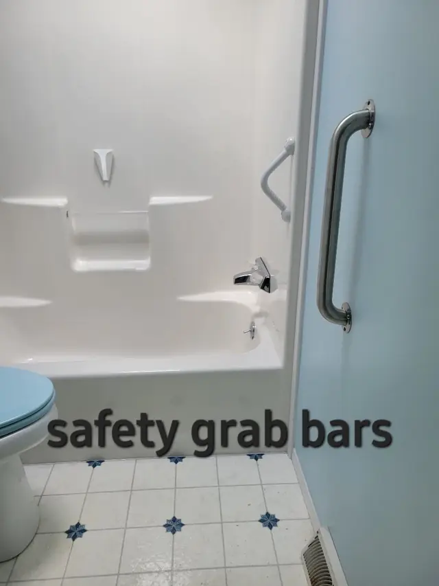 A stainless safety grab bar mounted on a pale blue bathroom wall beside a white tub