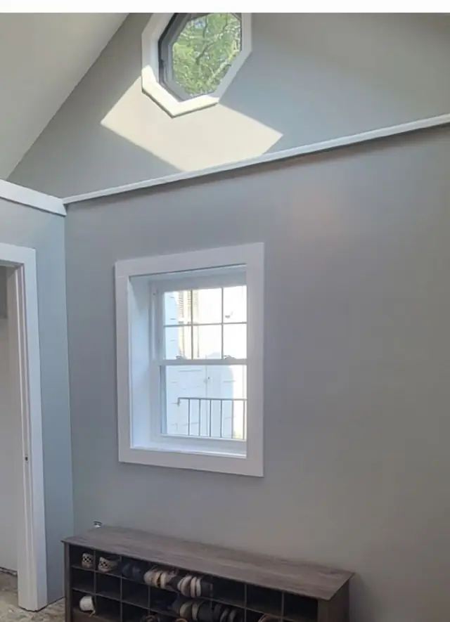 A grey room with a new trimmed window where a slider used to be, a shoe bench beneath it